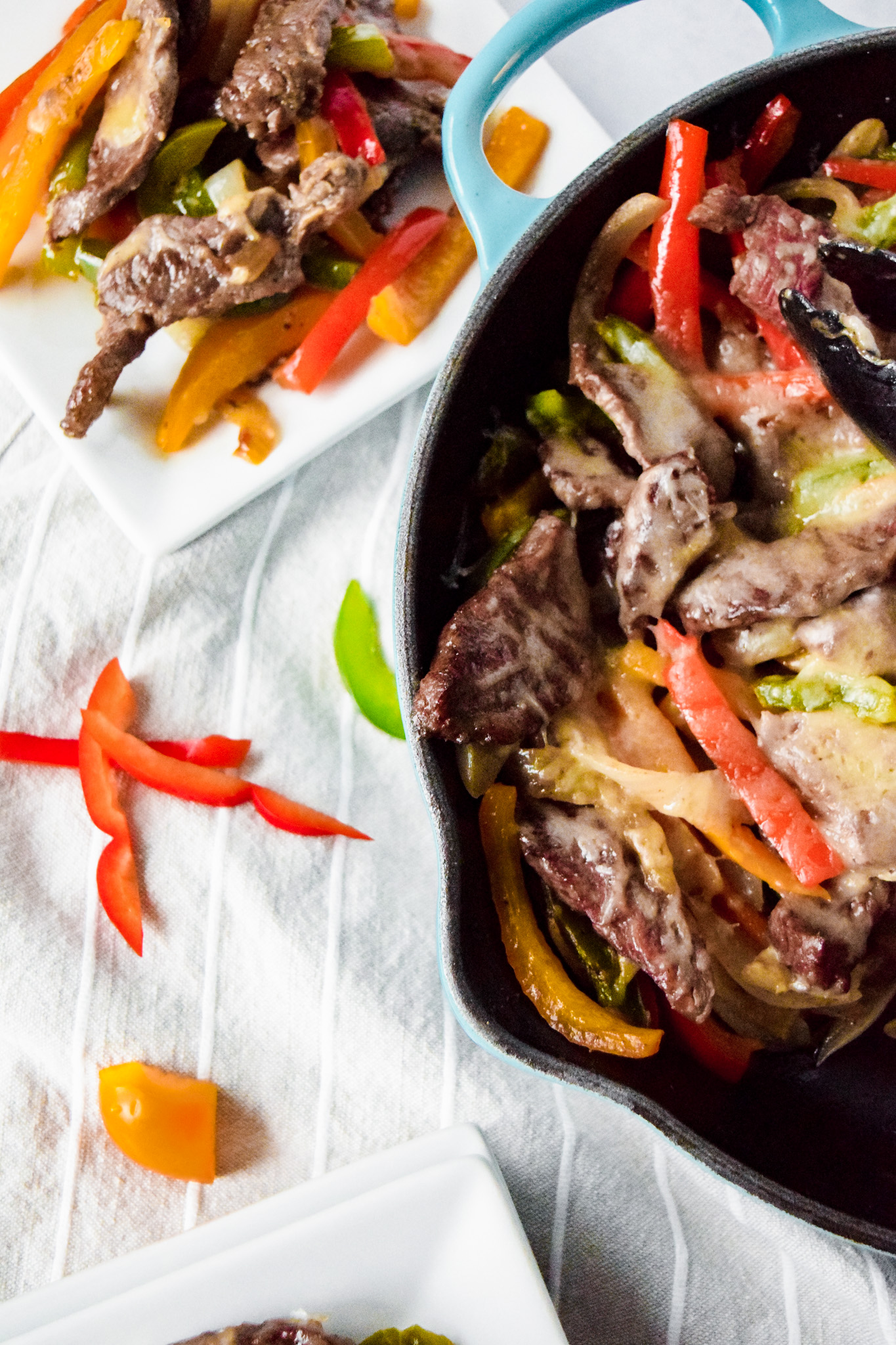 Le creuset teal skillet with sautéed steak, peppers, and onions