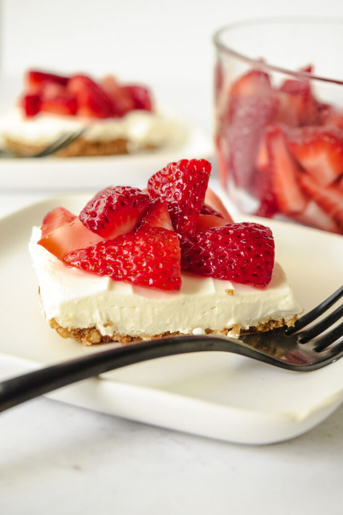 Slice of Gluten Free Strawberry Pretzel Salad on a white plate with a black fork