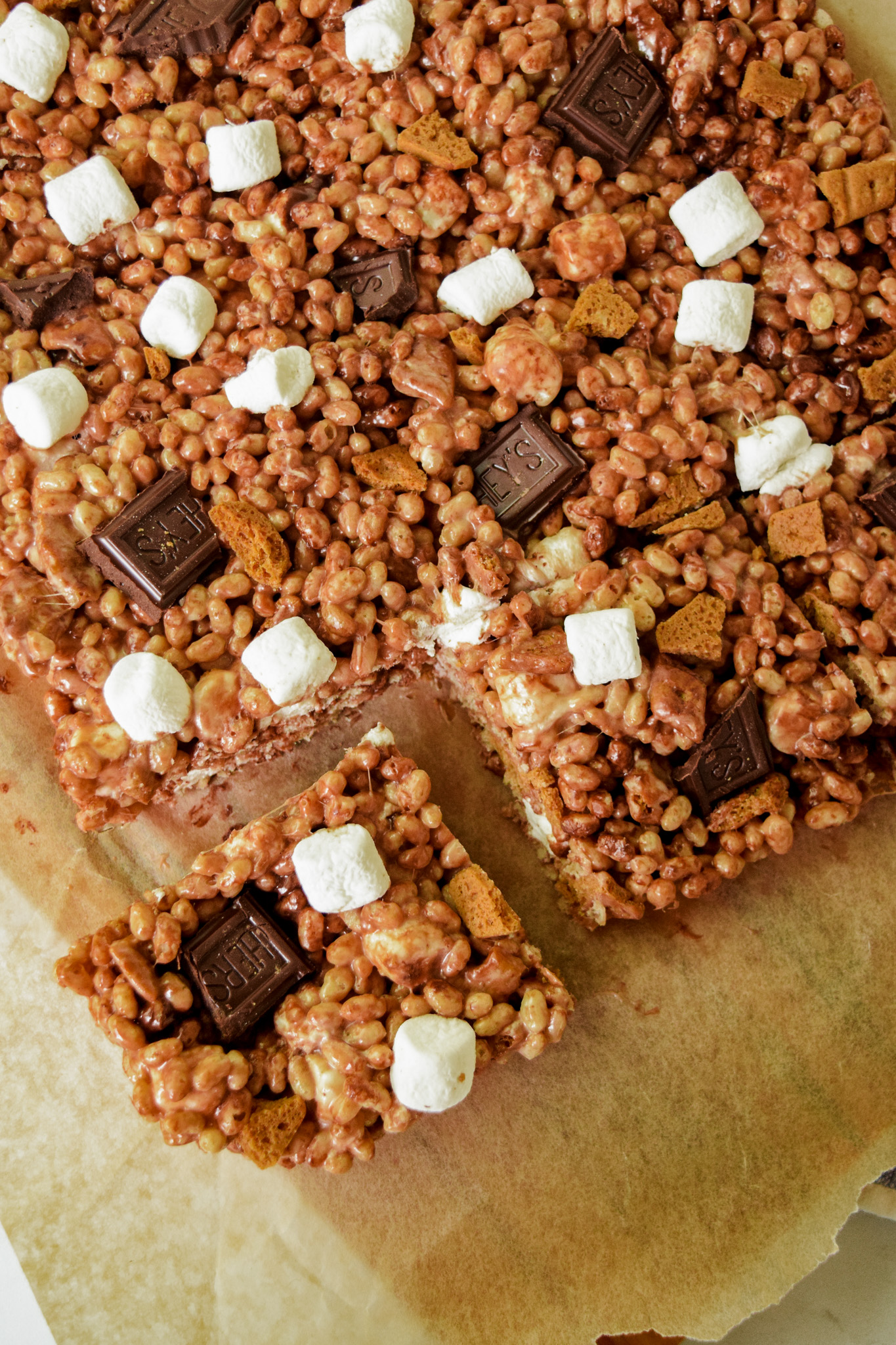 GF S'mores Cereal Treats with Chopped Hershey's milk chocolate, mini marshmallows, and graham cracker pieces on parchment paper
