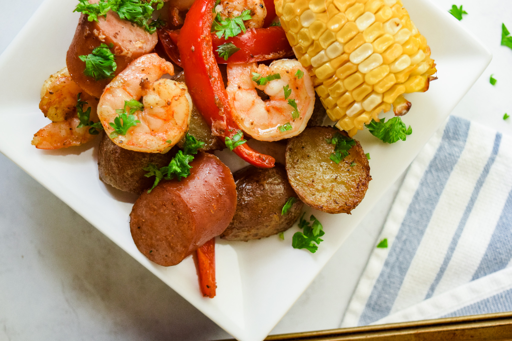Roasted Shrimp, Sausage, Red Peppers, Potatoes, Corn, and Parsley on a square white dinner plate