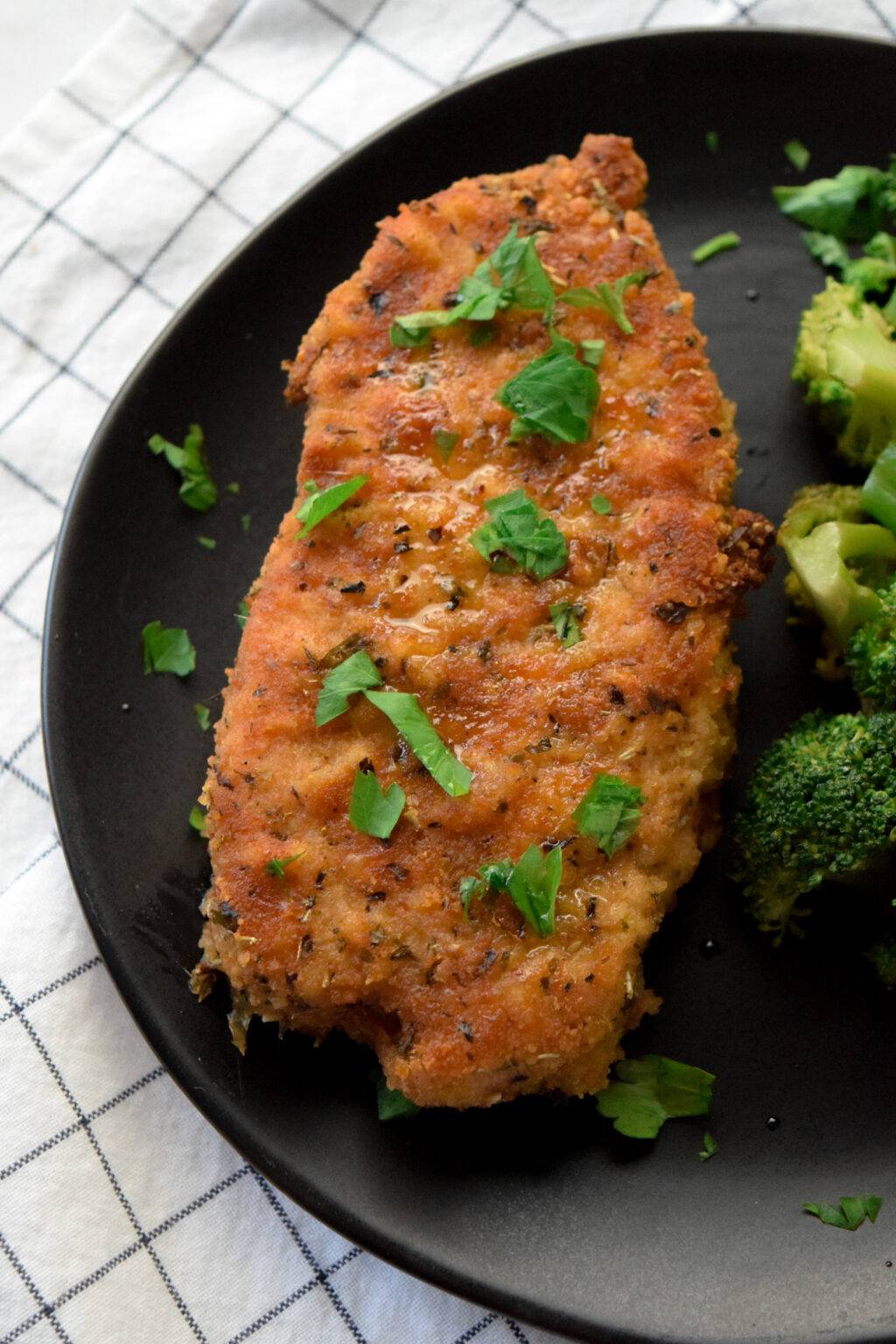breaded gluten free pork chops on a black plate with broccoli